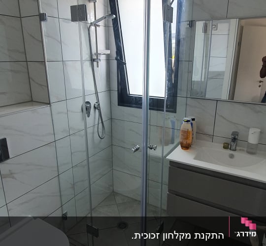 מקלחון זכוכית עם ראש מקלחת מתכתי וקירות אריחים לבנים